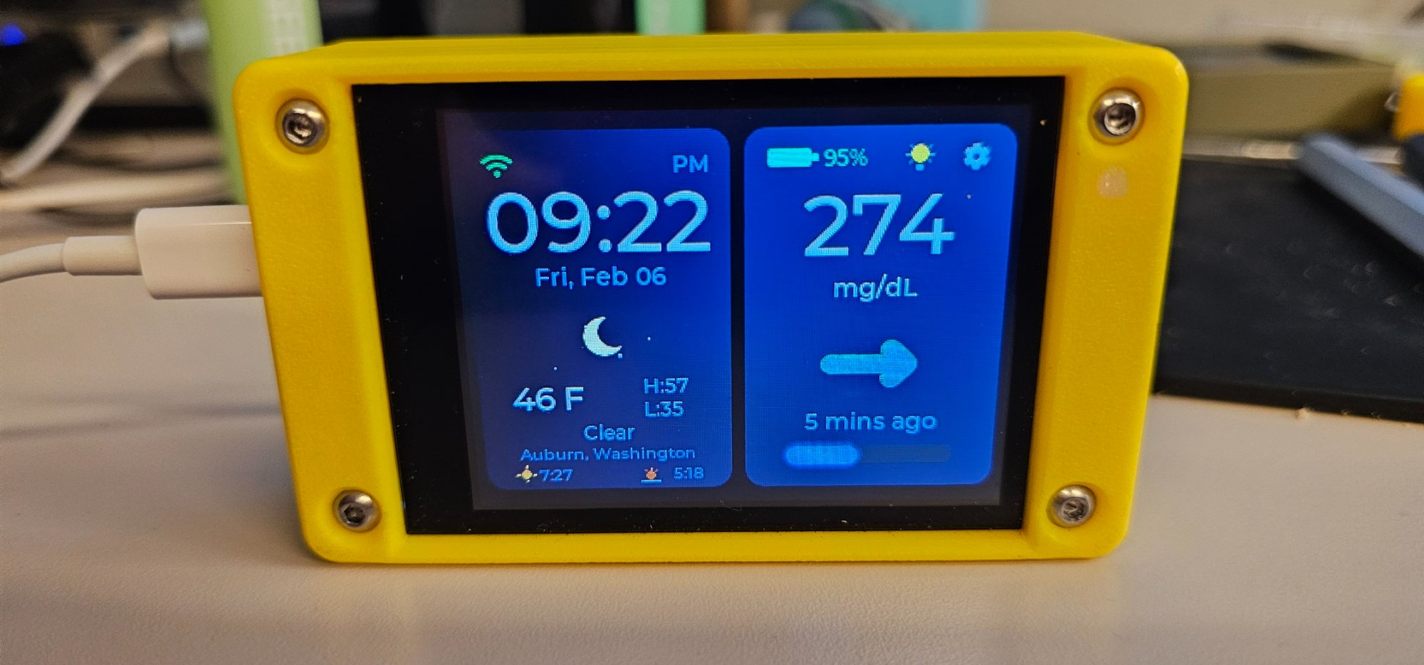 A CYGM display on a desk in a dark room, its glucose reading clearly legible without lighting the space around it.