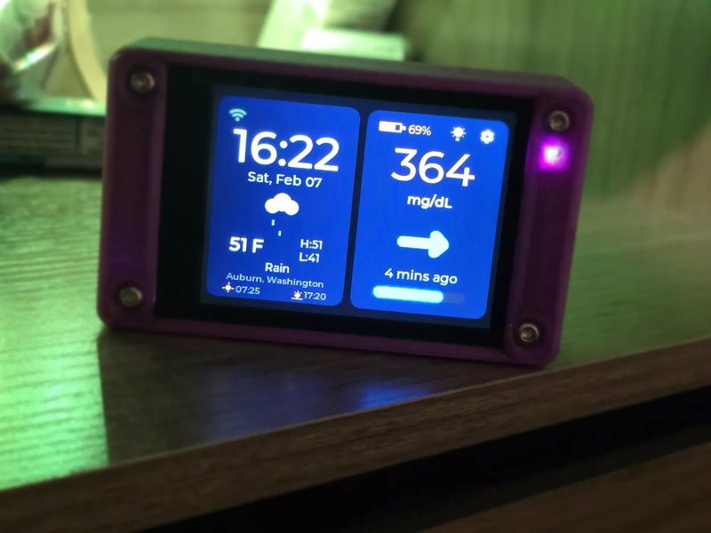 A close three-quarter view of a CYGM in a purple printed case on a wooden surface washed in green light, the screen filling the frame with 364 mg/dL and a 69 percent battery, and the violet status LED visible on the right edge.