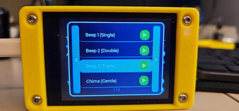 A CYGM in a yellow printed case on a desk, showing the alarm tone chooser with Beep 1, Beep 2, Beep 3 and Chime, each with a green play button.